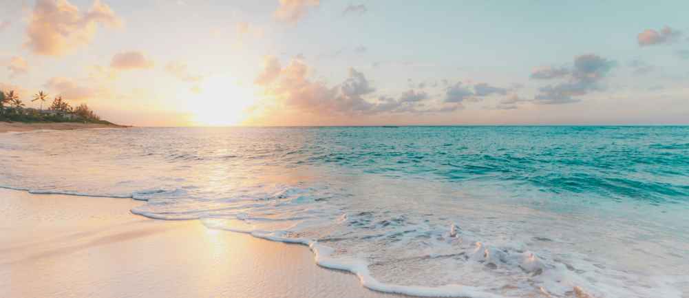 Zdjęcie przedstawia plażę i fale oceanu na tle zachodzącego słońca. 
