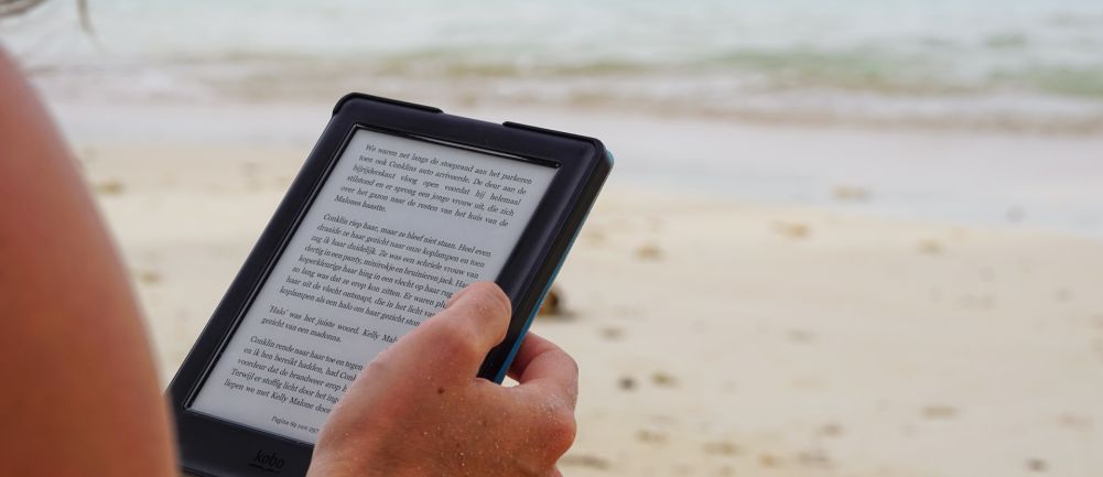 Kobieta siedząca na plaży i czytająca ebooka na czytniku