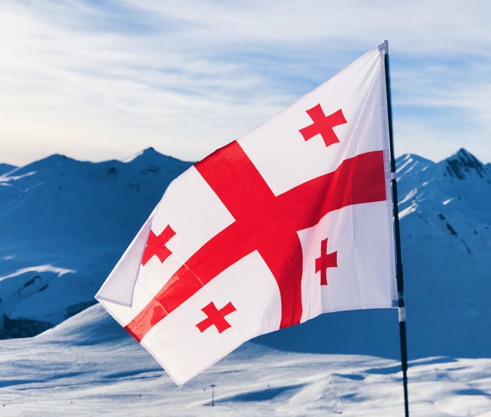 Flaga Gruzji wbita w śnieg na szczycie górskim. 