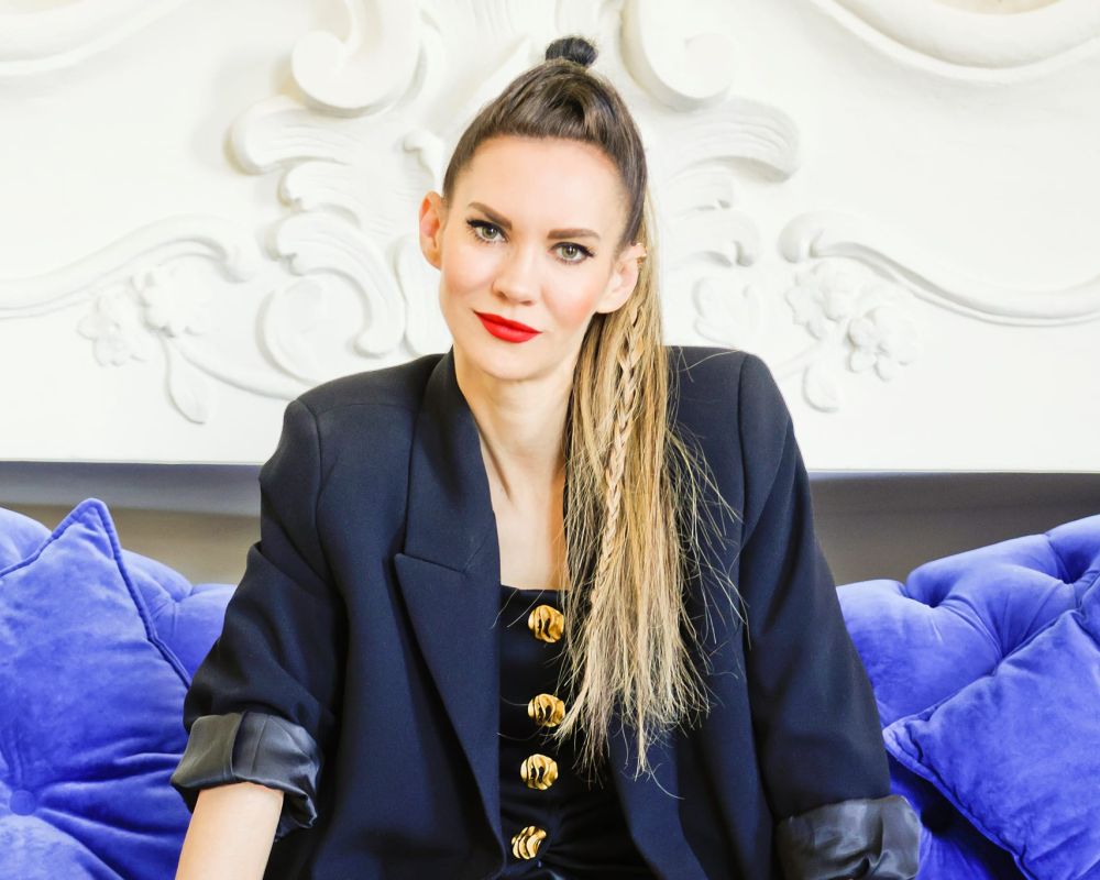 Małgorzata Sobczak - młoda kobieta w długich blond włosach, z warkoczem, siedząca na niebieskiej kanapie.