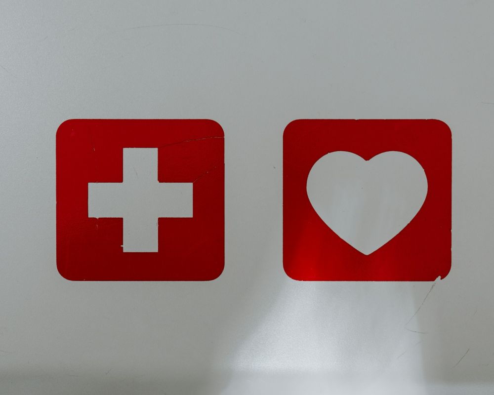 Na białym tle znaki medyczne: biały krzyż na czerwonym tle oraz białe serce na czerwonym tle 