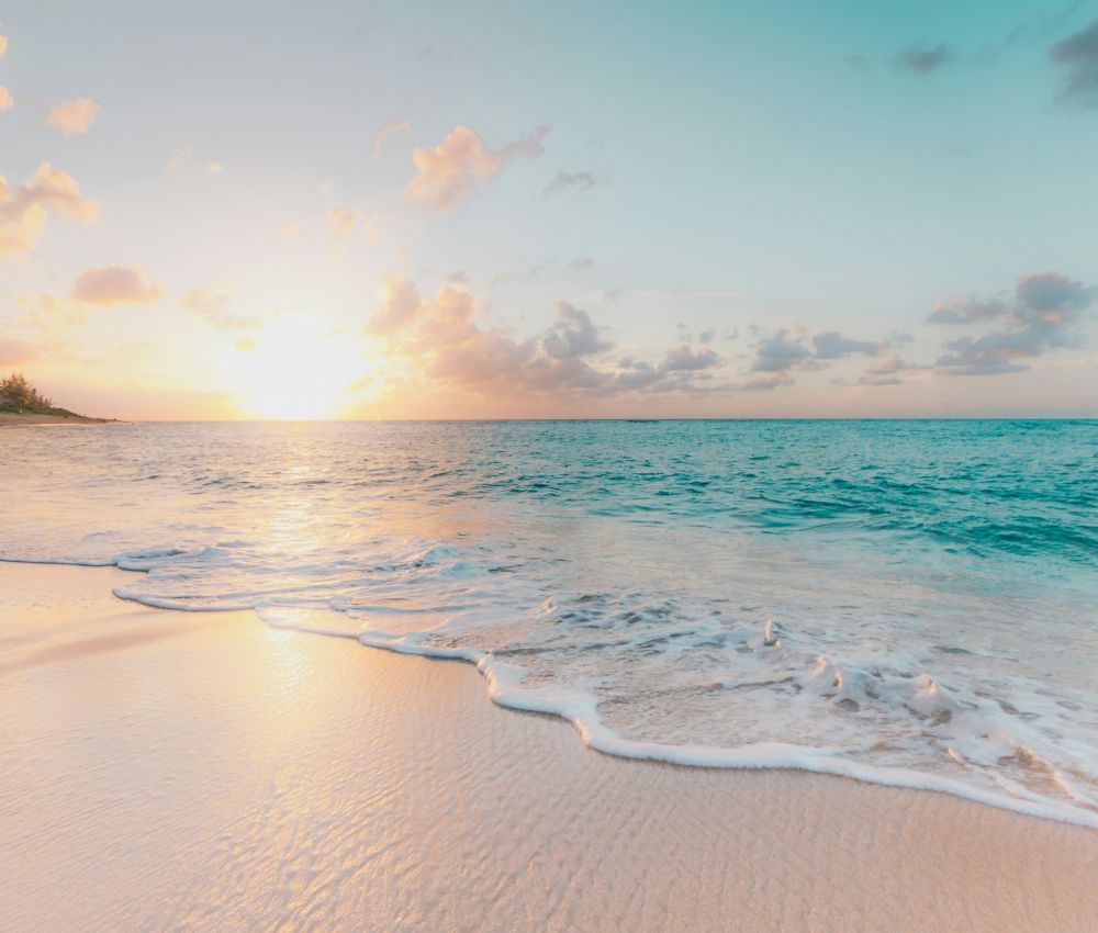 Zdjęcie przedstawia plażę i fale oceanu na tle zachodzącego słońca. 