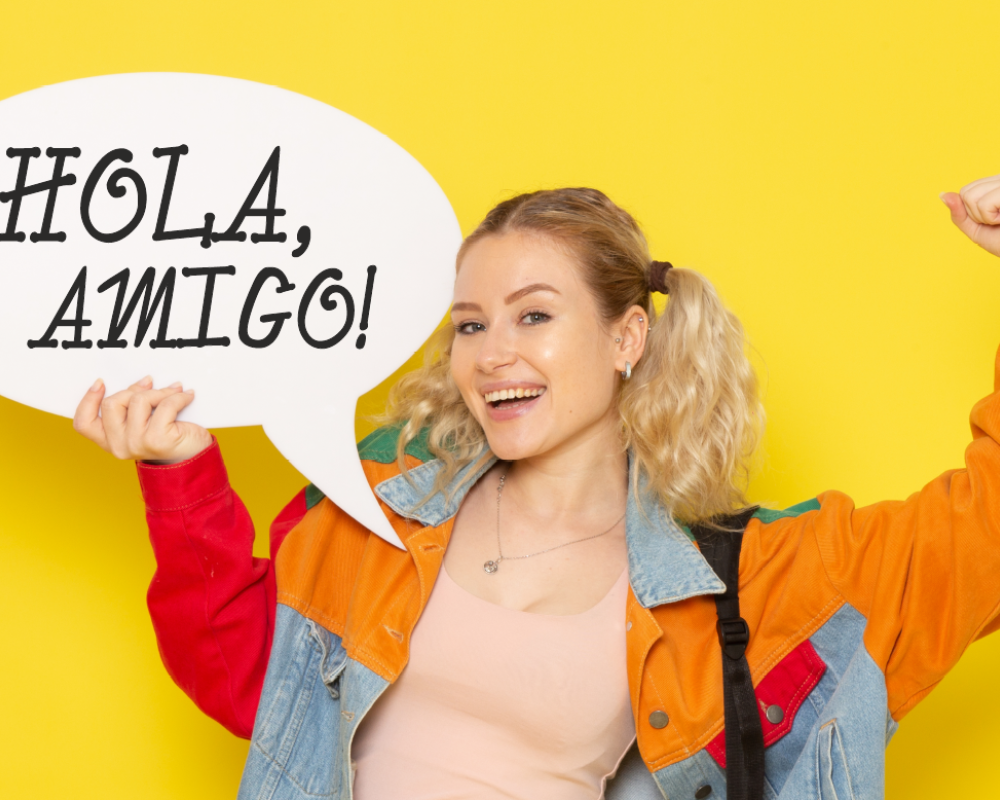 Ilustracja przedstawia młodą kobietę, trzymającą w prawej dłoni komiksowy dymek z napisem "Hola, amigo!", lewą rękę ma uniesioną w górę z zaciśniętą pięścią w geście radości..