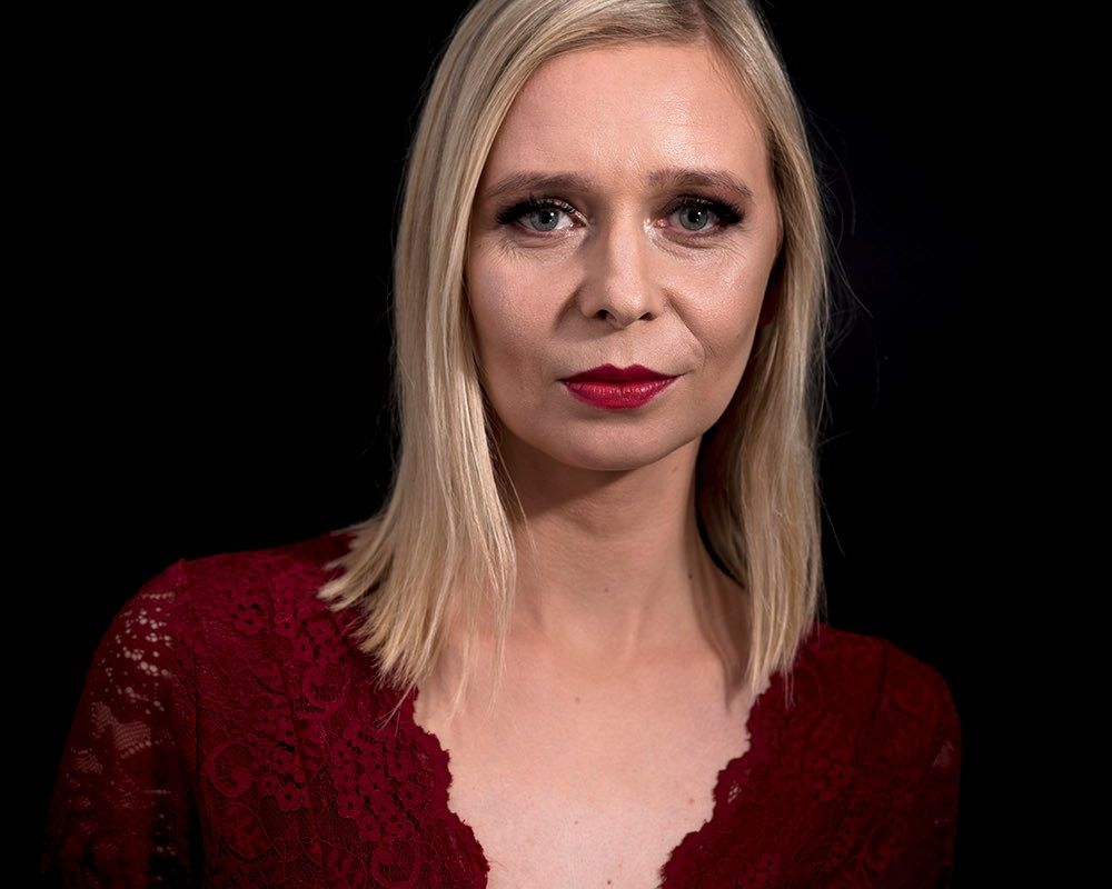 Zuzanna Gajewska. Młoda kobieta w blond włosach i czerwonej bluzce. Ma pomalowane usta czerwoną szminką.