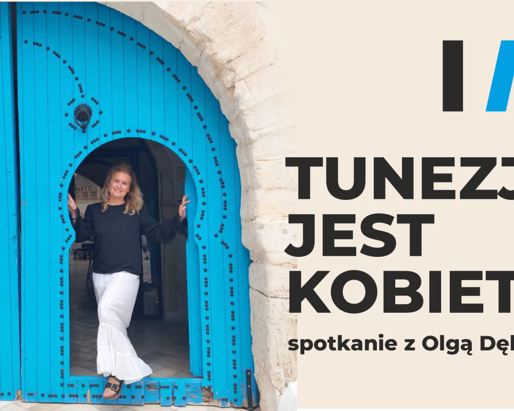 Olga Dębicka wypatruje zza niebieskiej bramy w budynku z kamienia