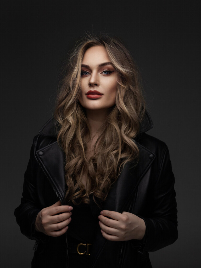 Młoda kobieta w długich blond włosach. Ma ubraną skórzaną kurtkę.