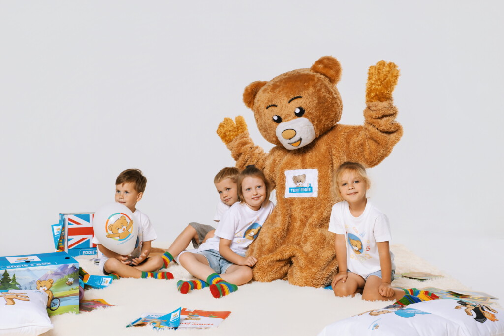 Duży brązowy miś, przy którym siedzą dzieci