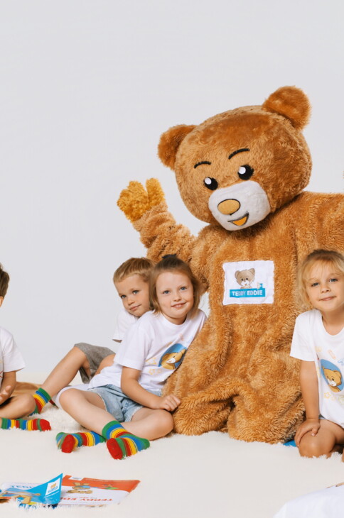 Duży brązowy miś, przy którym siedzą dzieci