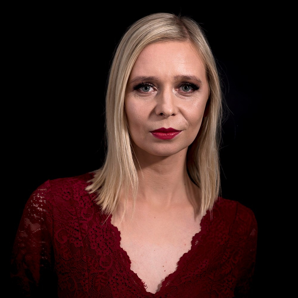 Zuzanna Gajewska. Młoda kobieta w blond włosach i czerwonej bluzce. Ma pomalowane usta czerwoną szminką.
