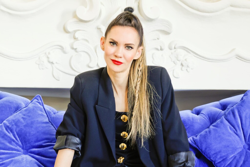 Małgorzata Sobczak - młoda kobieta w długich blond włosach, z warkoczem, siedząca na niebieskiej kanapie.