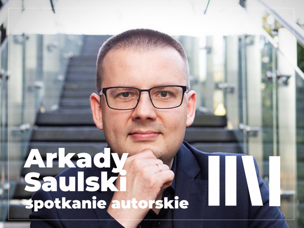 Arkady Saulski w ciemnej koszuli, z okularami na nosie. Za nim schody.