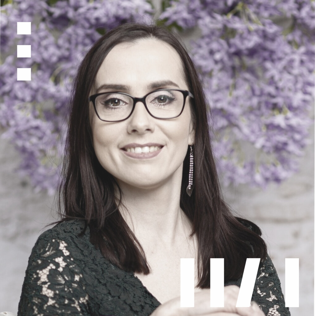 Anna Ziobro - młoda kobieta, w dłuższych, ciemnych włosach. Ma ubrane okulary z ciemnymi oprawkami. Siedzi na obróconym, białym krześle.
