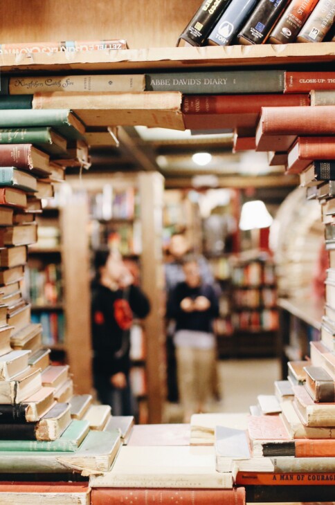 biblioteczna półka z książkami, w których tle widać sylwetki ludzi