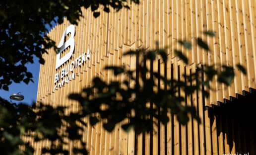 Biblioteka Witomino z zewnątrz. Elewacja z drewnianymi lamelami. W rogu budynku białe logo Biblioteki Gdynia