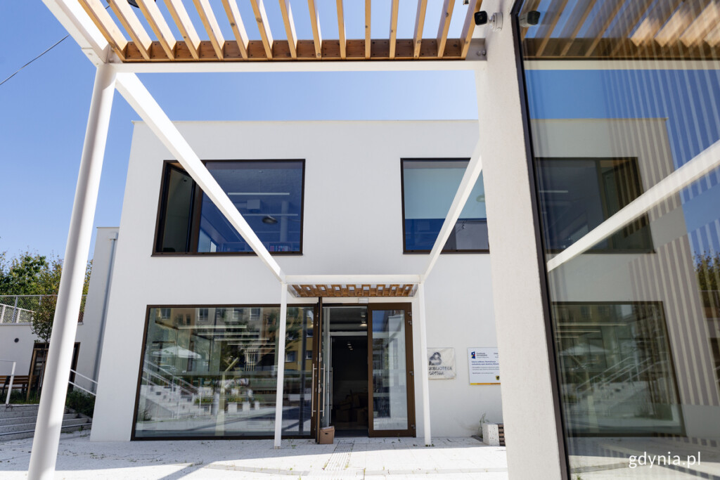 Biblioteka Witomino z zewnątrz, od strony głównego wejścia. Prostokątny, biały budynek z dużymi oknami.