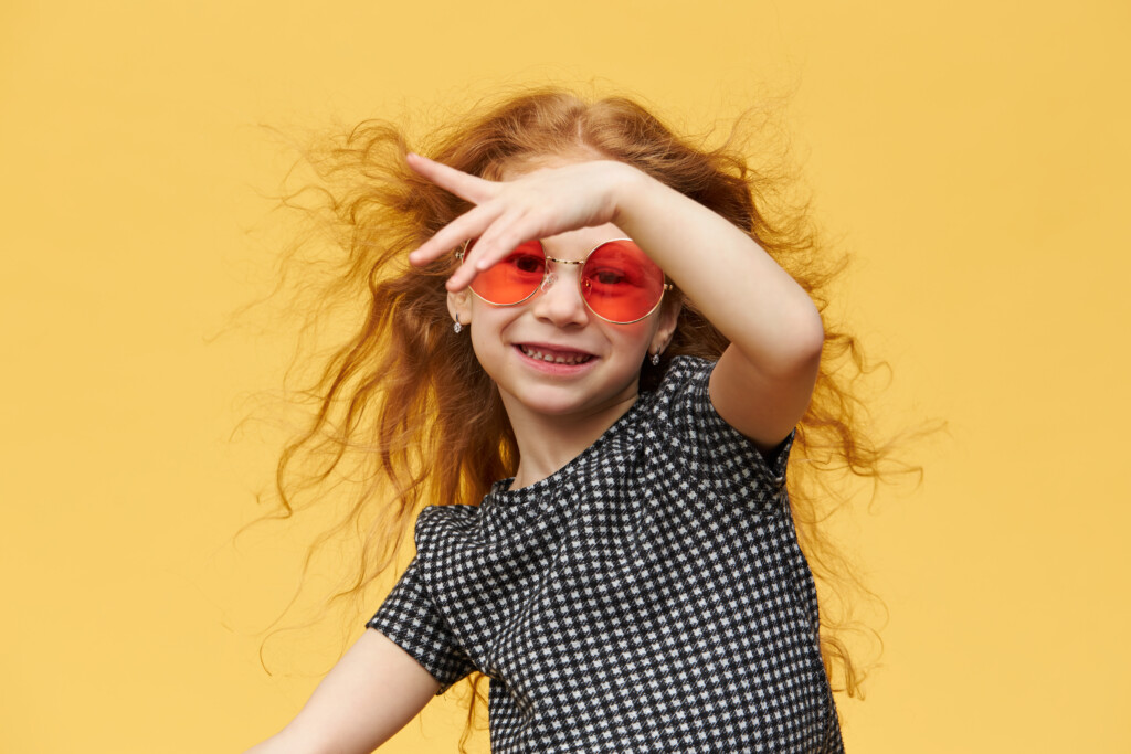 horizontal-shot-of-beautiful-happy-trendy-little-girl-with-curly-ginger-hair-enjoying-dancing-with-cheerful-broad-smile-wearing-sunglasses-music-dance-fun-and-children-concept