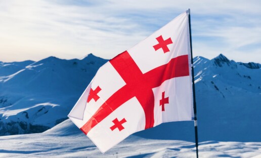 Flaga Gruzji wbita w śnieg na szczycie górskim.