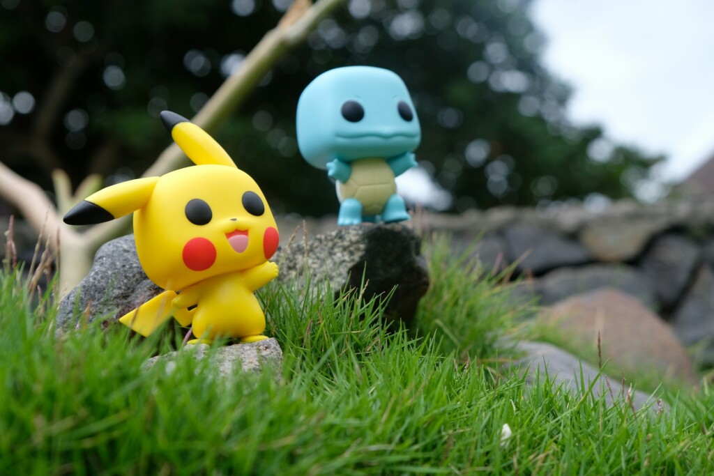 Figurki Pokemonów stojące na kamieniach leżących na trawie.