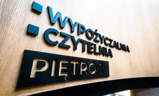 Czarny napis na drewnianej ściance "Wypożyczalnia. Czytelnia. Piętro 1"