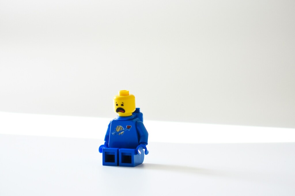 Płaczący ludzik z klocków LEGO. Jest w pozycji siedzącej. Ma niebieską bluzę i spodnie. Białe tło.