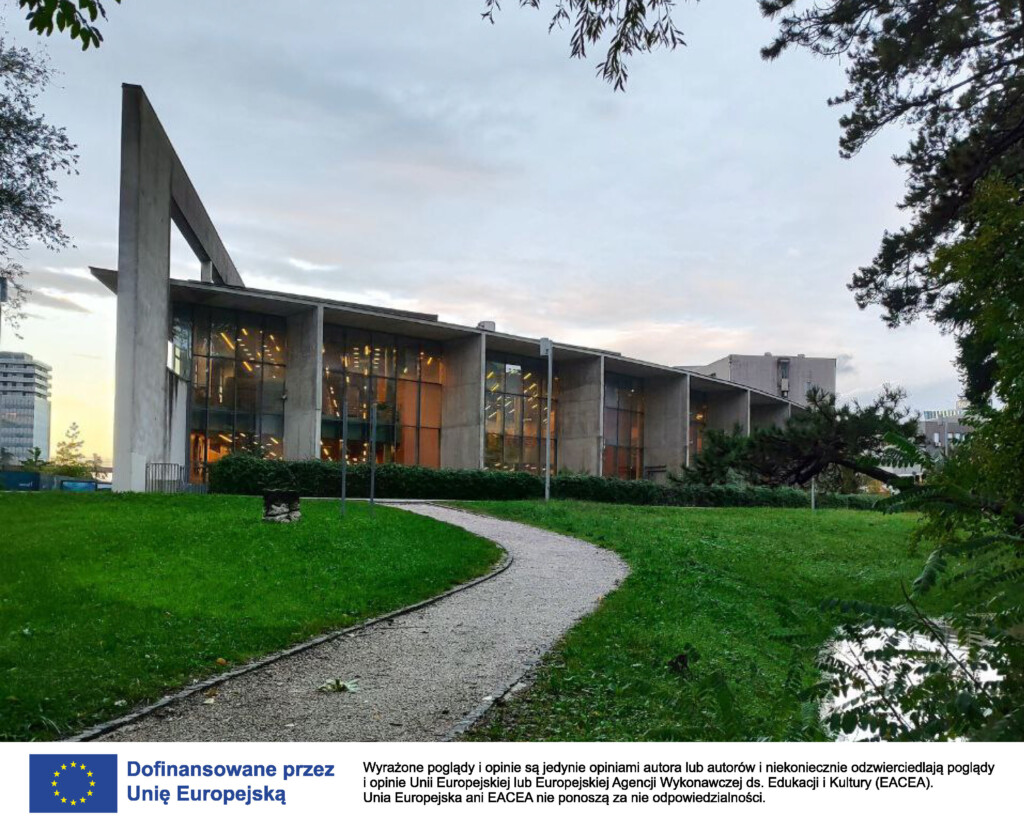 Zdjęcie przedstawia gmach biblioteki w Novej Goricy, w Słowenii. Przed budynkiem widać równoskoszoną trawę i prowadzącą do biblioteki drogę.