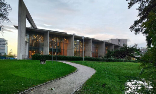 Zdjęcie przedstawia gmach biblioteki w Novej Goricy, w Słowenii. Przed budynkiem widać równoskoszoną trawę i prowadzącą do biblioteki drogę.