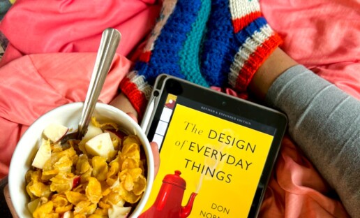 Na różowej pościeli leży miska z owsianką oraz czytnik ebooków. Widać też nogi siedzącej osoby na łóżku osoby..