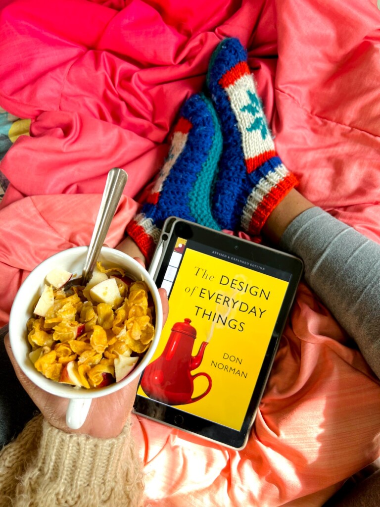 Na różowej pościeli leży miska z owsianką oraz czytnik ebooków. Widać też nogi siedzącej osoby na łóżku osoby..
