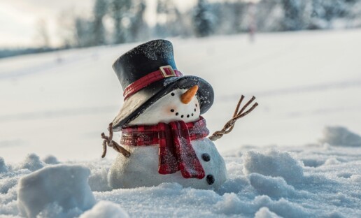 Bałwanek stojący na śniegu. Ma cylinder na głowie i czerwony szalik w kratę przewiązany wokół szyi.