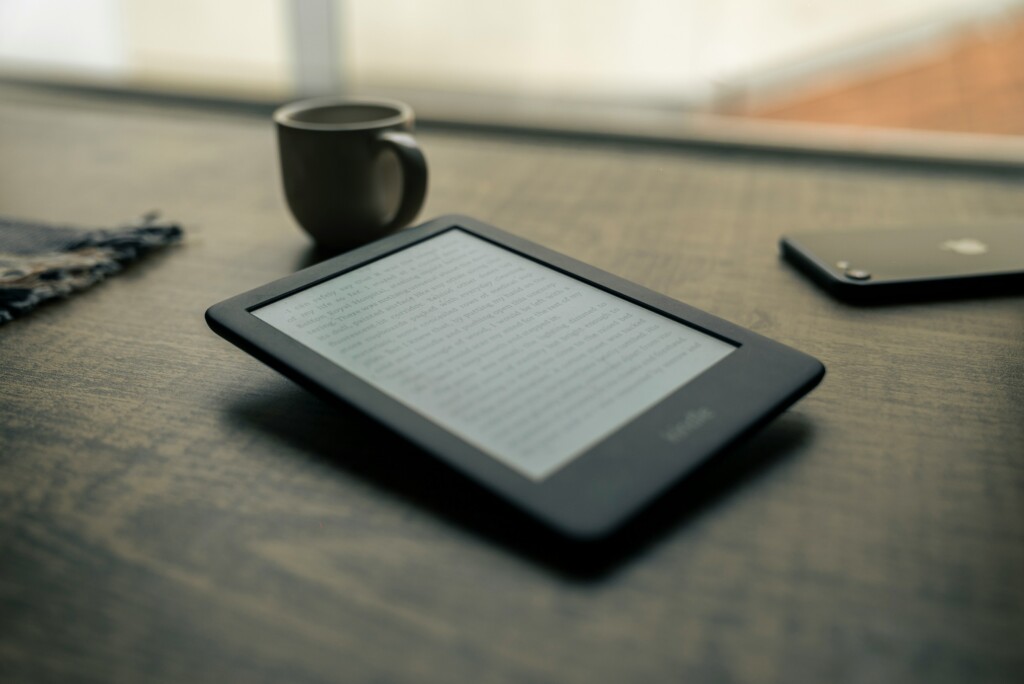 Czytnik ebooków leżący na stole. W tle widać kubek i telefon.
