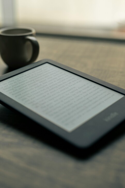 Czytnik ebook&oacute;w leżący na stole. W tle widać kubek i telefon.