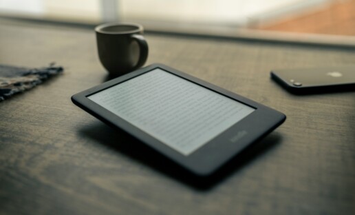 Czytnik ebooków leżący na stole. W tle widać kubek i telefon.