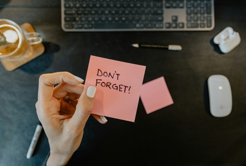 Dłoń trzymająca różową karteczkę z napisem "Don't forget"