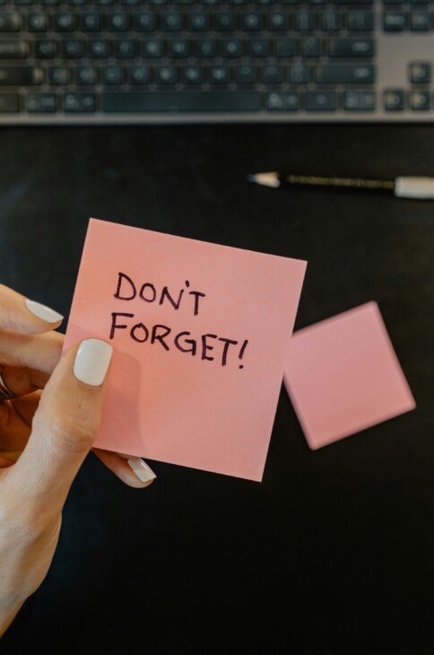 Dłoń trzymająca różową karteczkę z napisem "Don't forget"