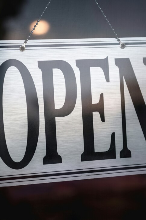 biała tabliczna z czarnym napisem "open" wywieszona na szybie